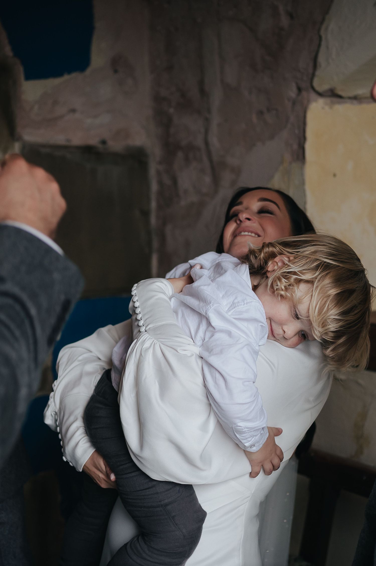 A child in white clothing hugs someone in a tender indoor moment.
