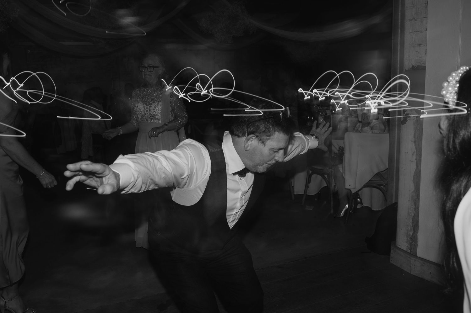 Wedding guest dancing energetically with light trails in background.
