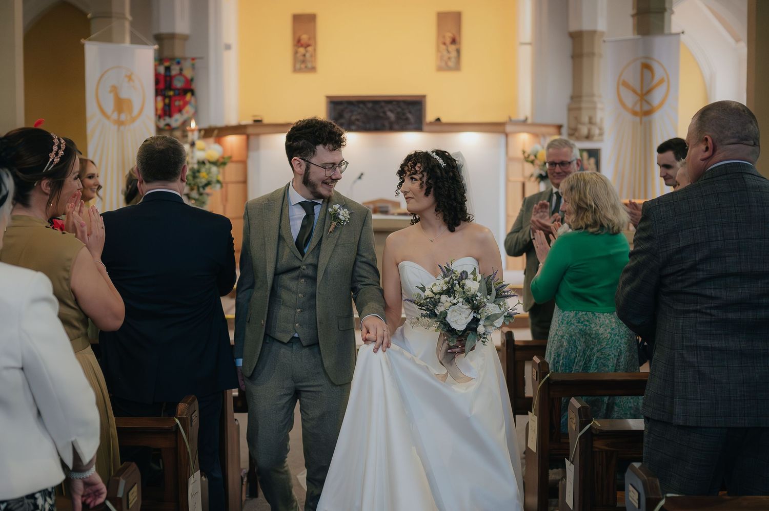 A wedding couple walking down the church aisle surrounded by guests during their ceremony.