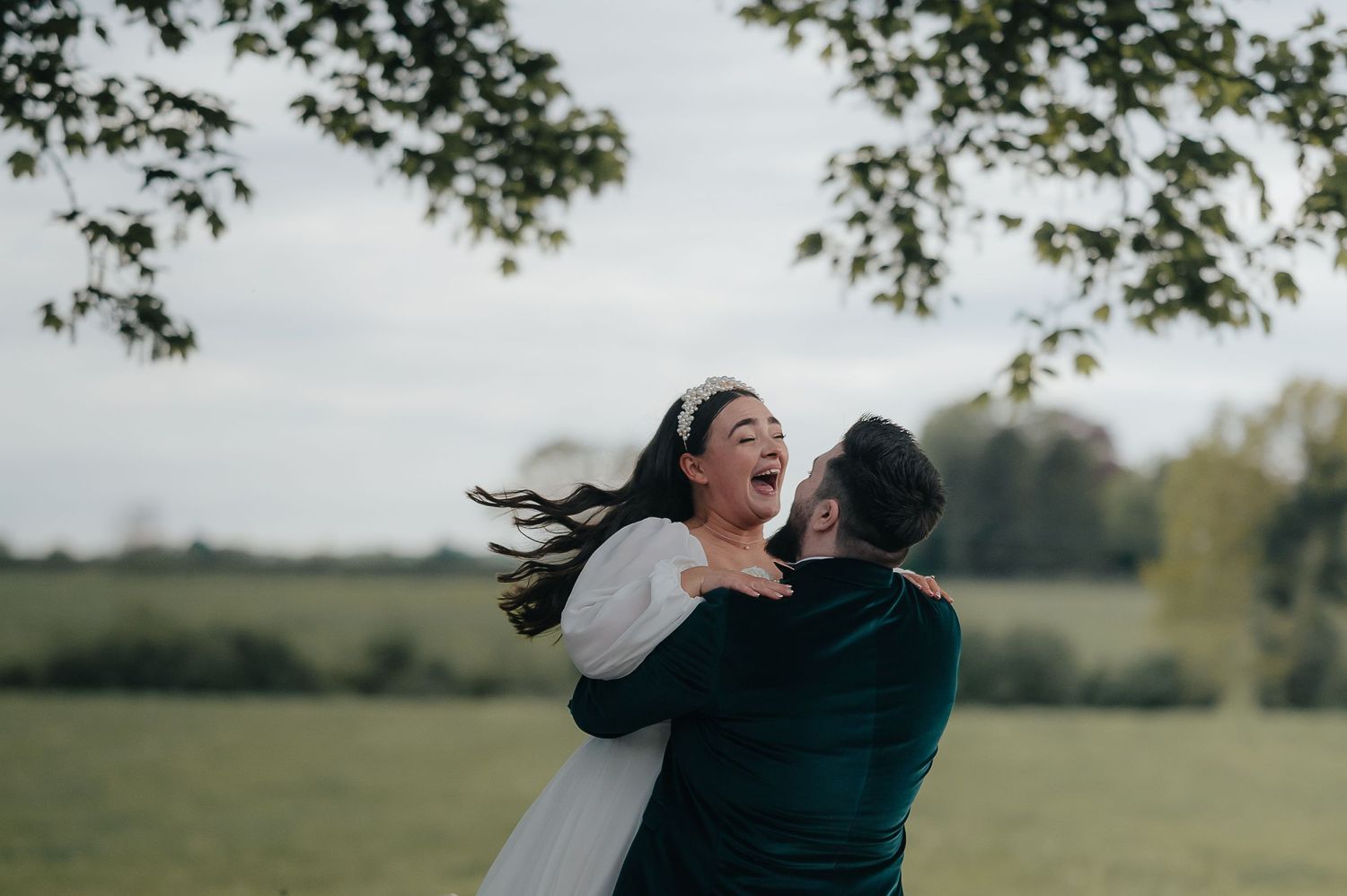 Joyful wedding couple spinning and laughing in a meadow.