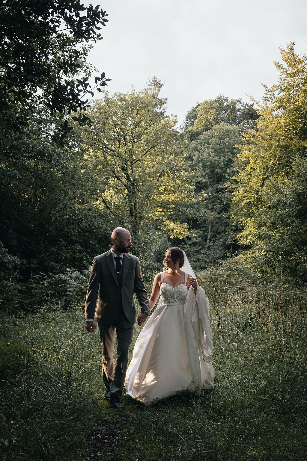 Wedding couple walking hand in hand on a nature trail surrounded by autumn trees.