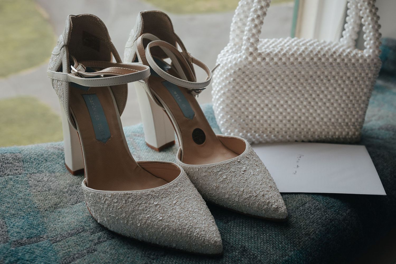 Elegant white lace wedding shoes with ankle straps displayed on a dark surface.