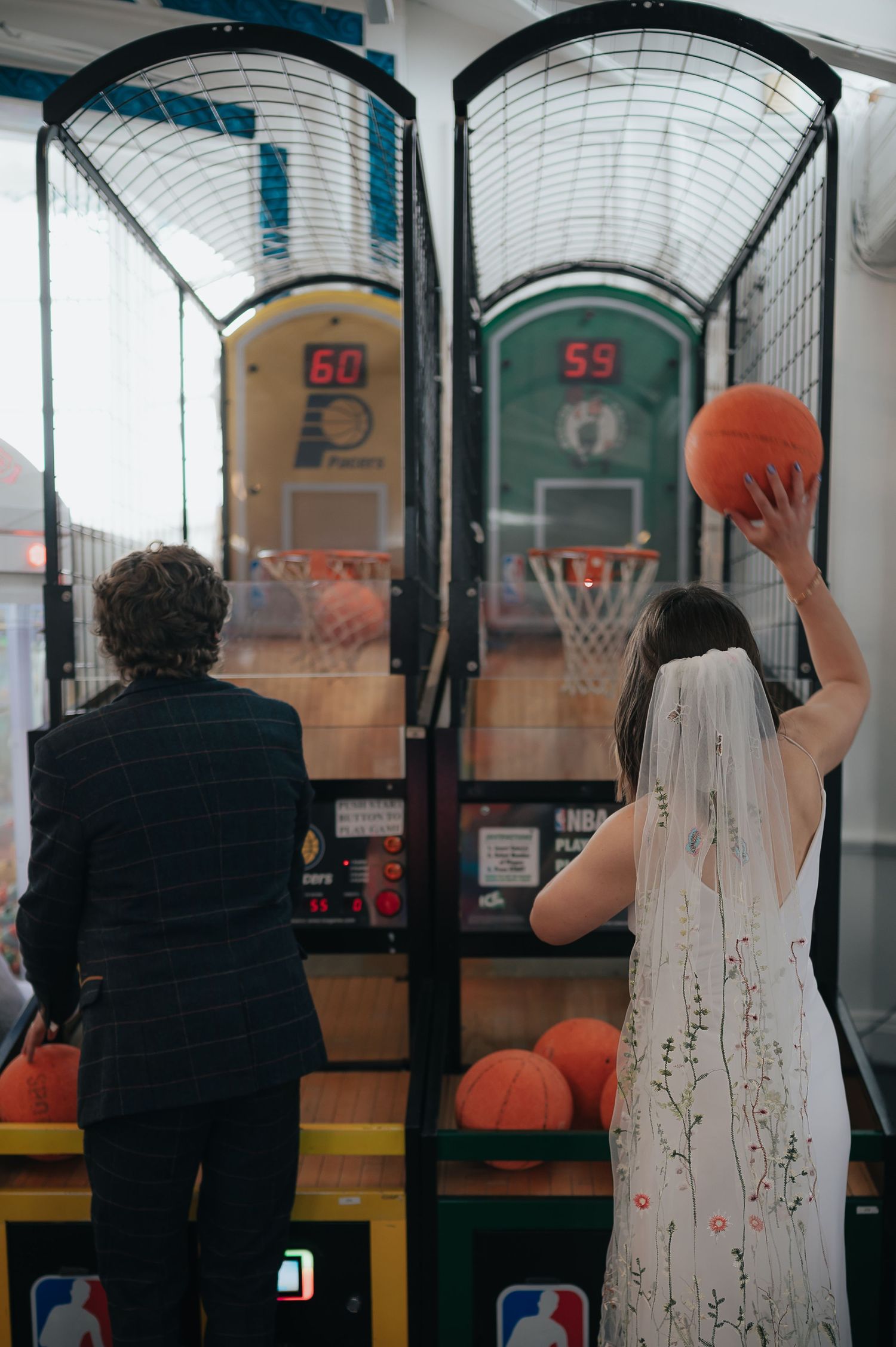 Couple in wedding attire playing basketball arcade game.