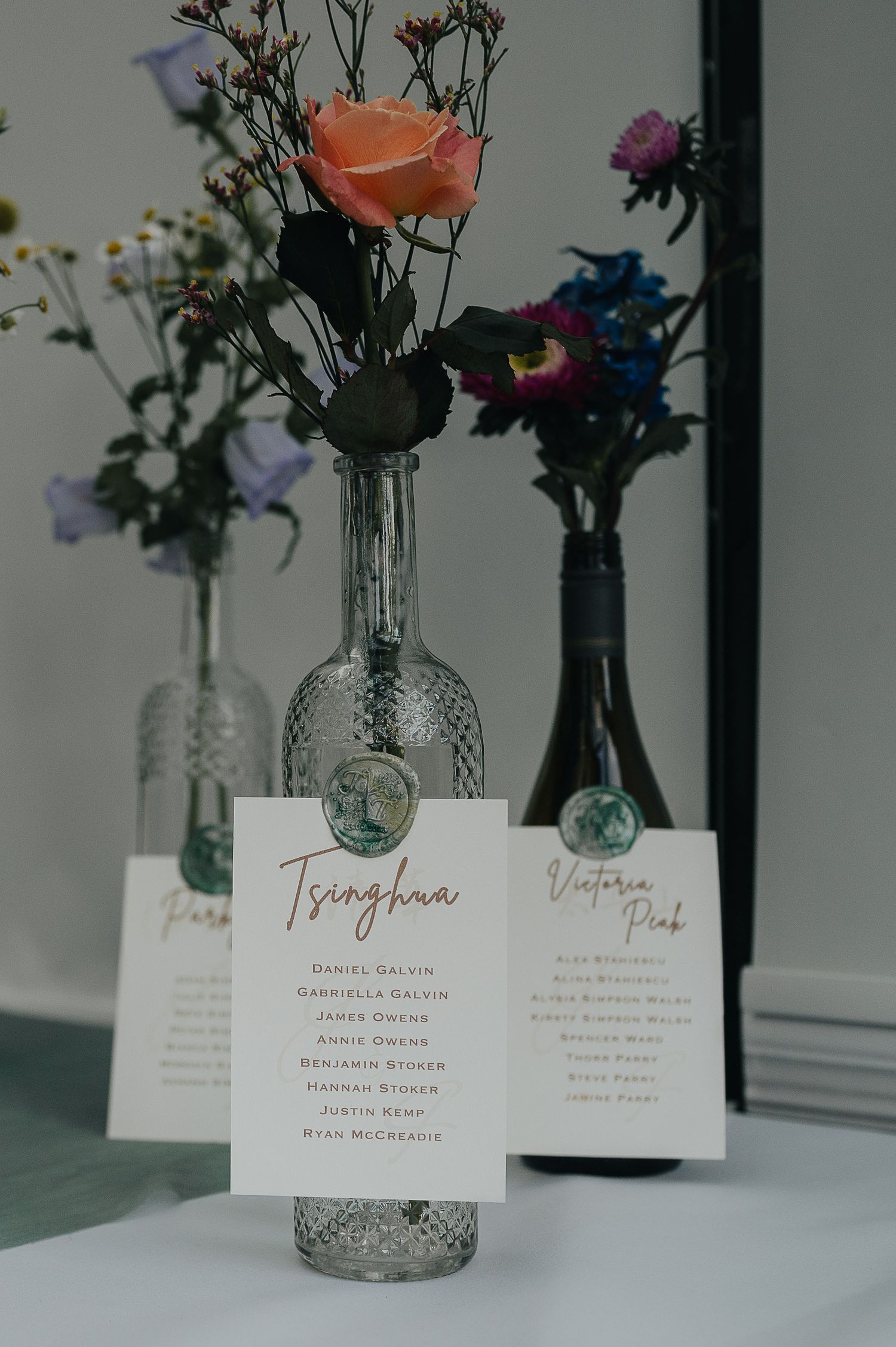 Wedding table cards displayed with floral arrangements in decorative glass bottles.
