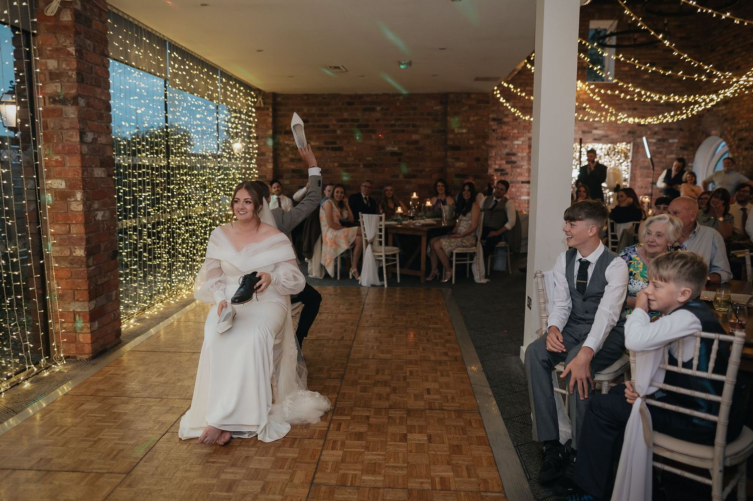 Wedding celebration on dance floor with fairy lights and exposed brick walls.