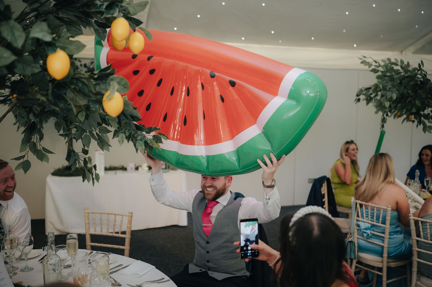 Guest at wedding reception holding up large inflatable watermelon slice decoration.