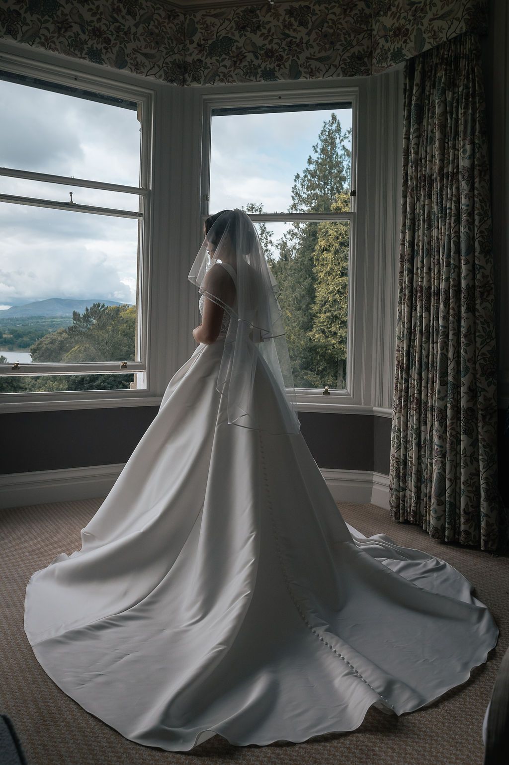 Wedding gown silhouette against bay windows with mountain view and dramatic clouds.