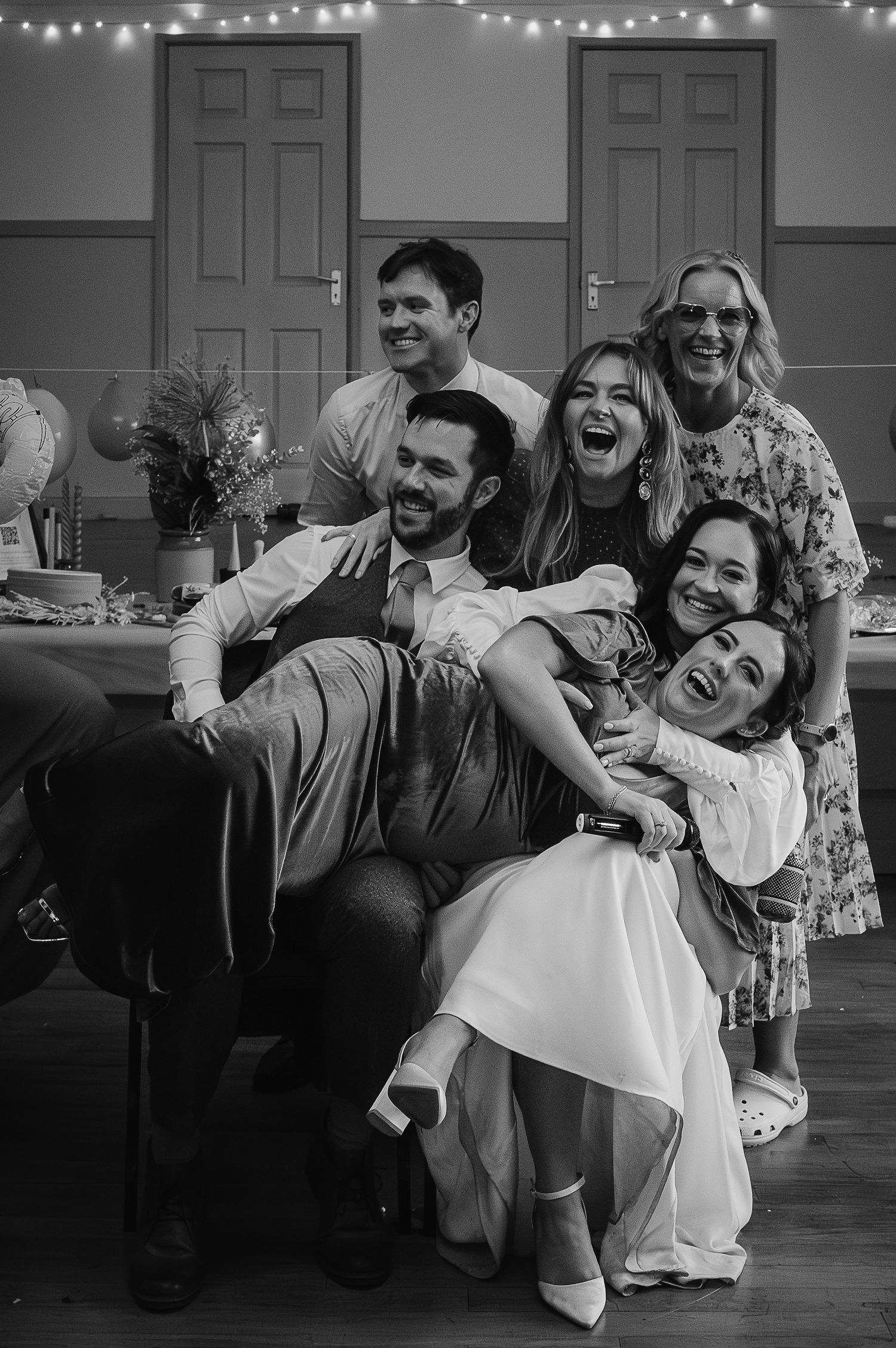 A joyful group celebrating at a wedding reception with string lights in the background.