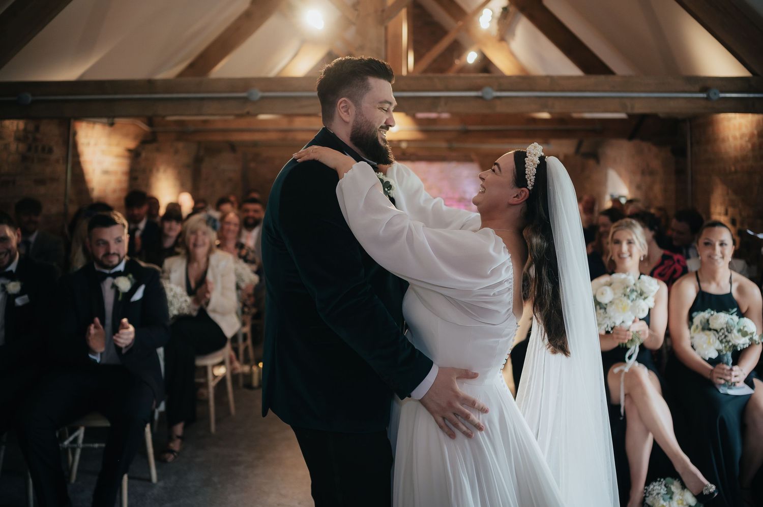 A romantic first dance moment in a rustic venue with exposed wooden beams and watching guests.