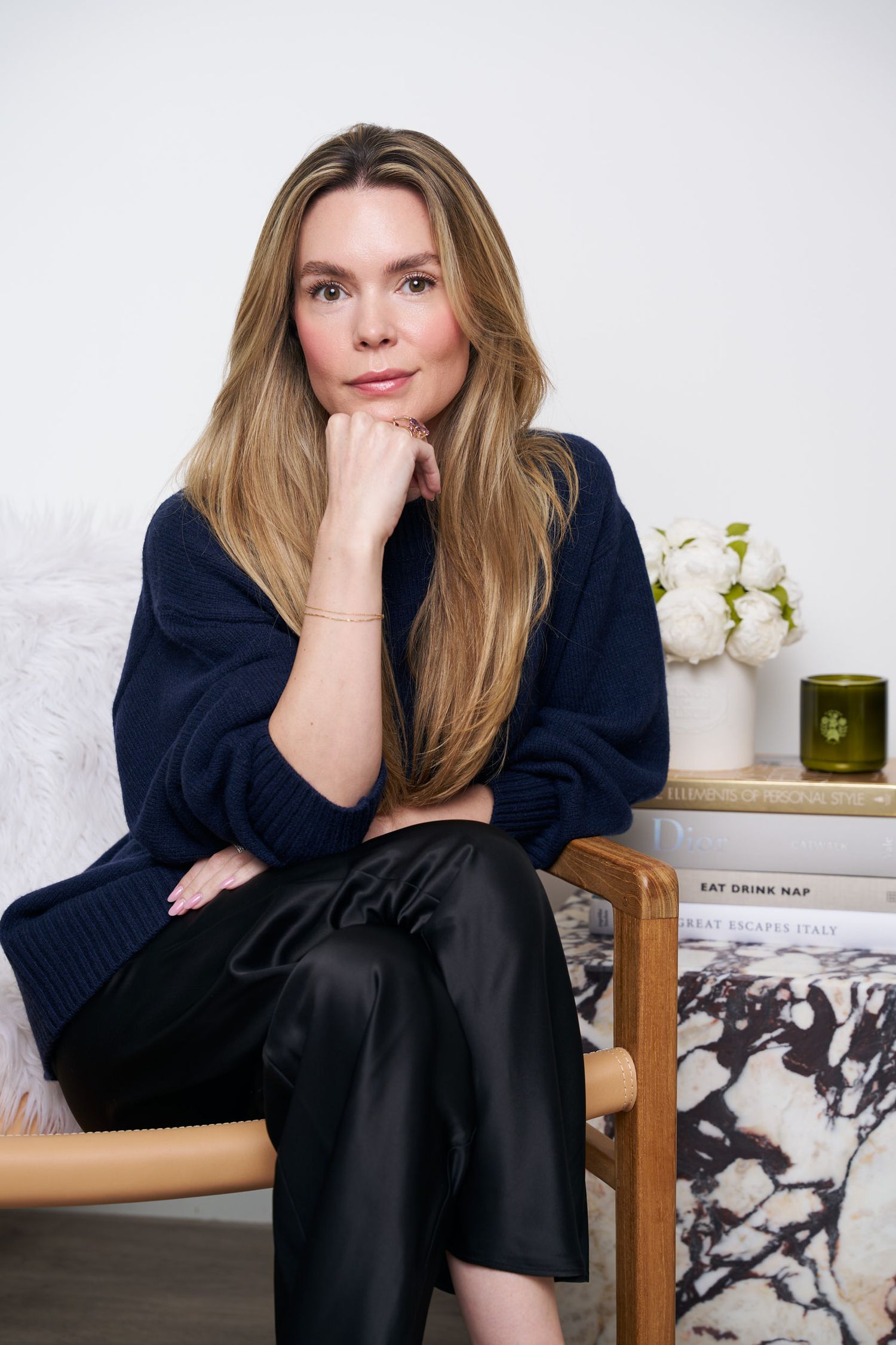 Person in a black sweater sits casually on wooden furniture against a white wall with floral decor.