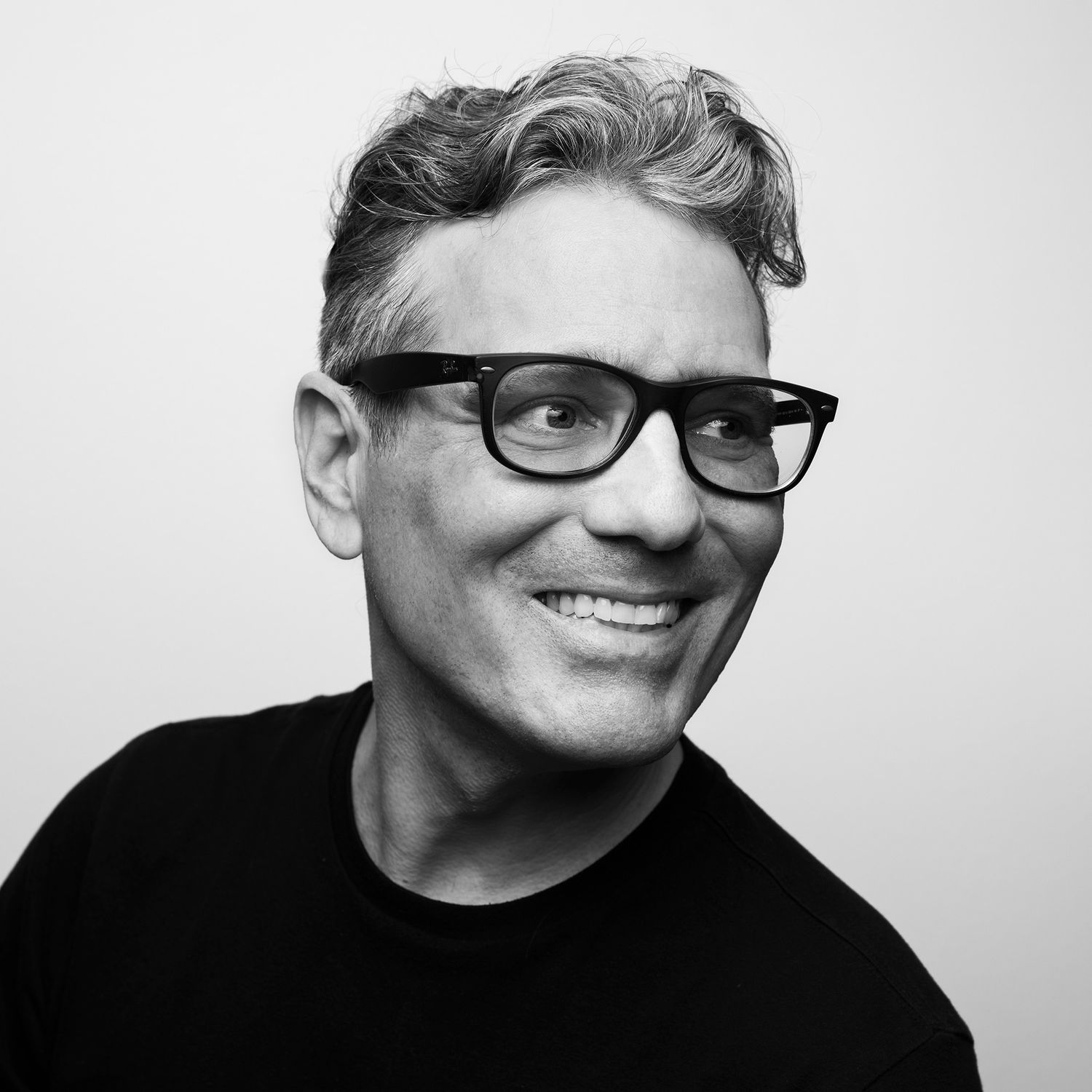 Black and white portrait series of a person wearing glasses against a dark background, shown in four different poses.