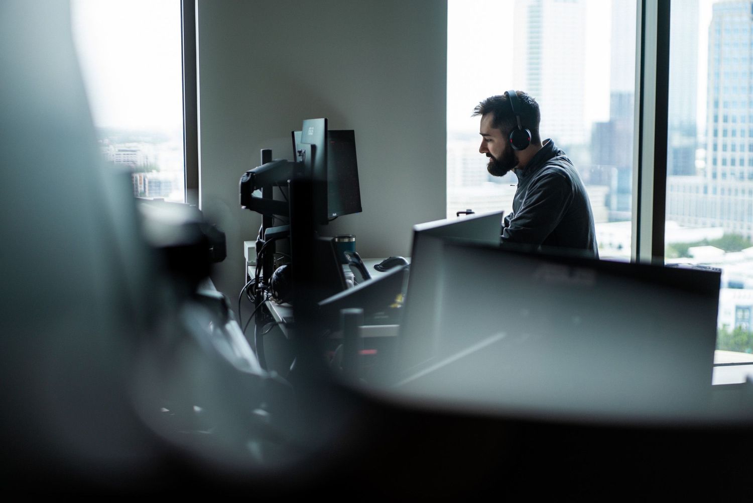 A sequence of dark silhouettes working at desks in an office space with natural light streaming through windows.