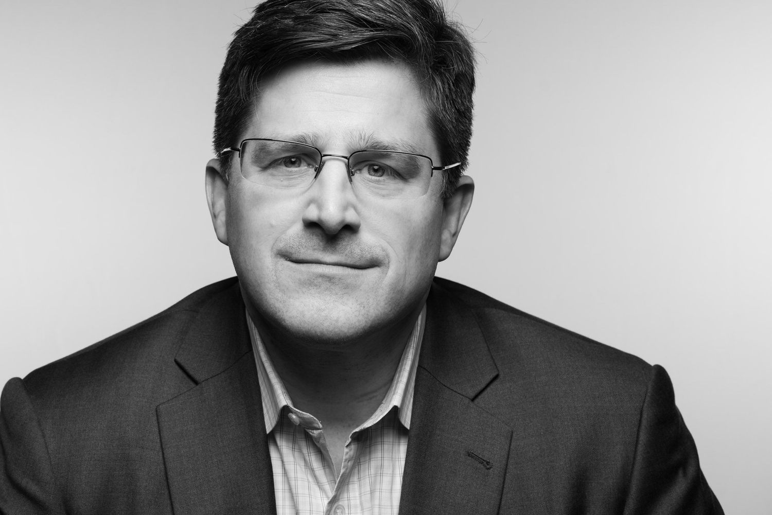 Professional black and white portrait of someone in business attire wearing glasses against a plain background.