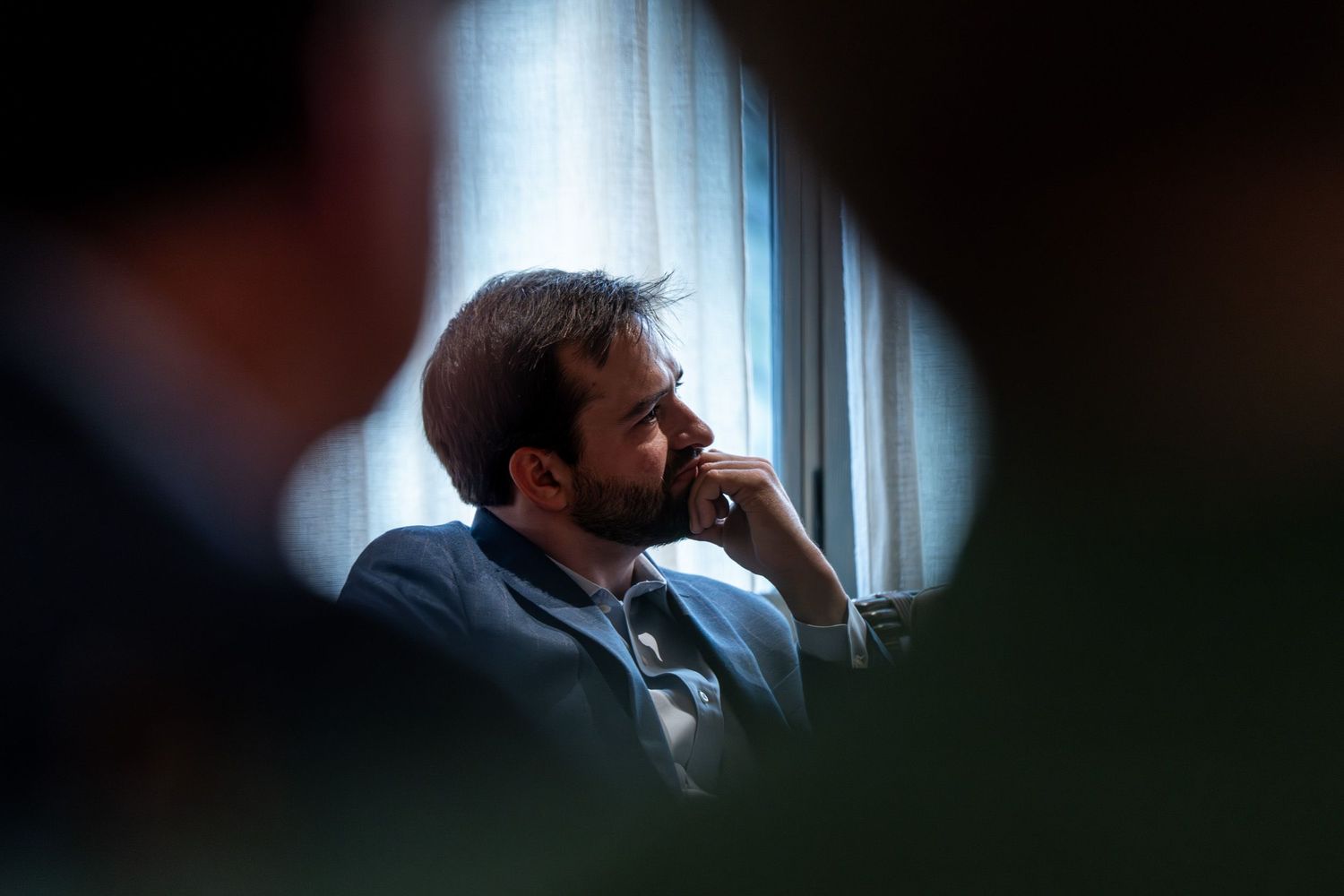 A contemplative person gazes thoughtfully out a window while sitting in shadow during a quiet moment.
