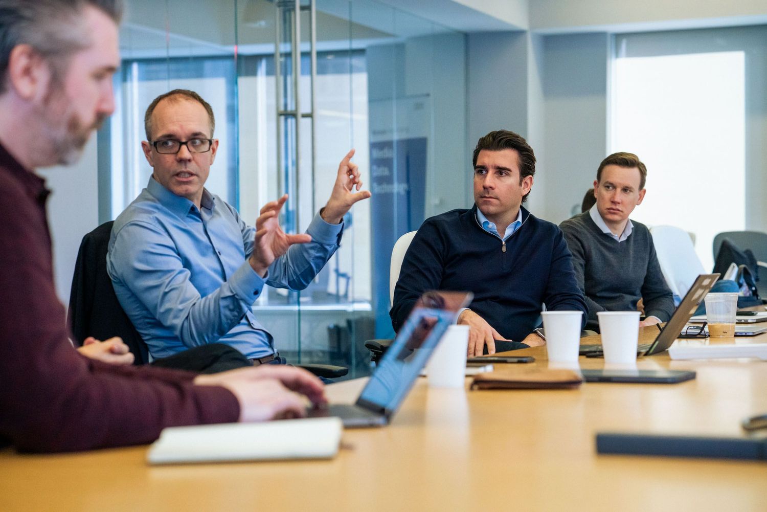Business professionals collaborate during a meeting in a modern conference room with glass walls and laptops.