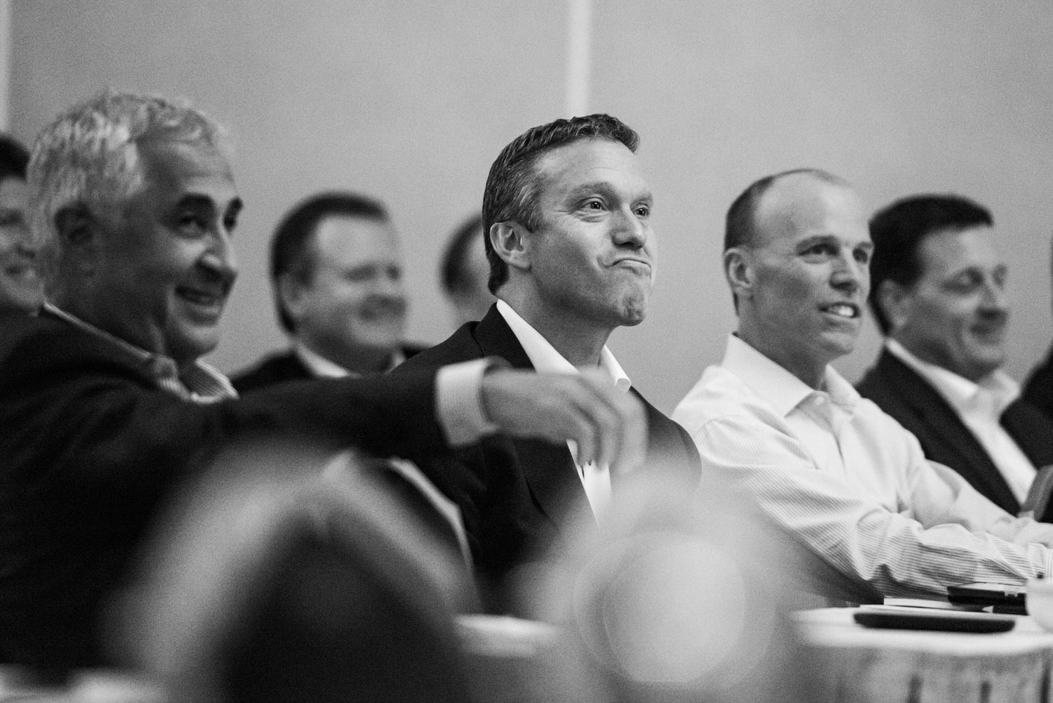A group of men in formal attire sit together at an event, shown in black and white photography.