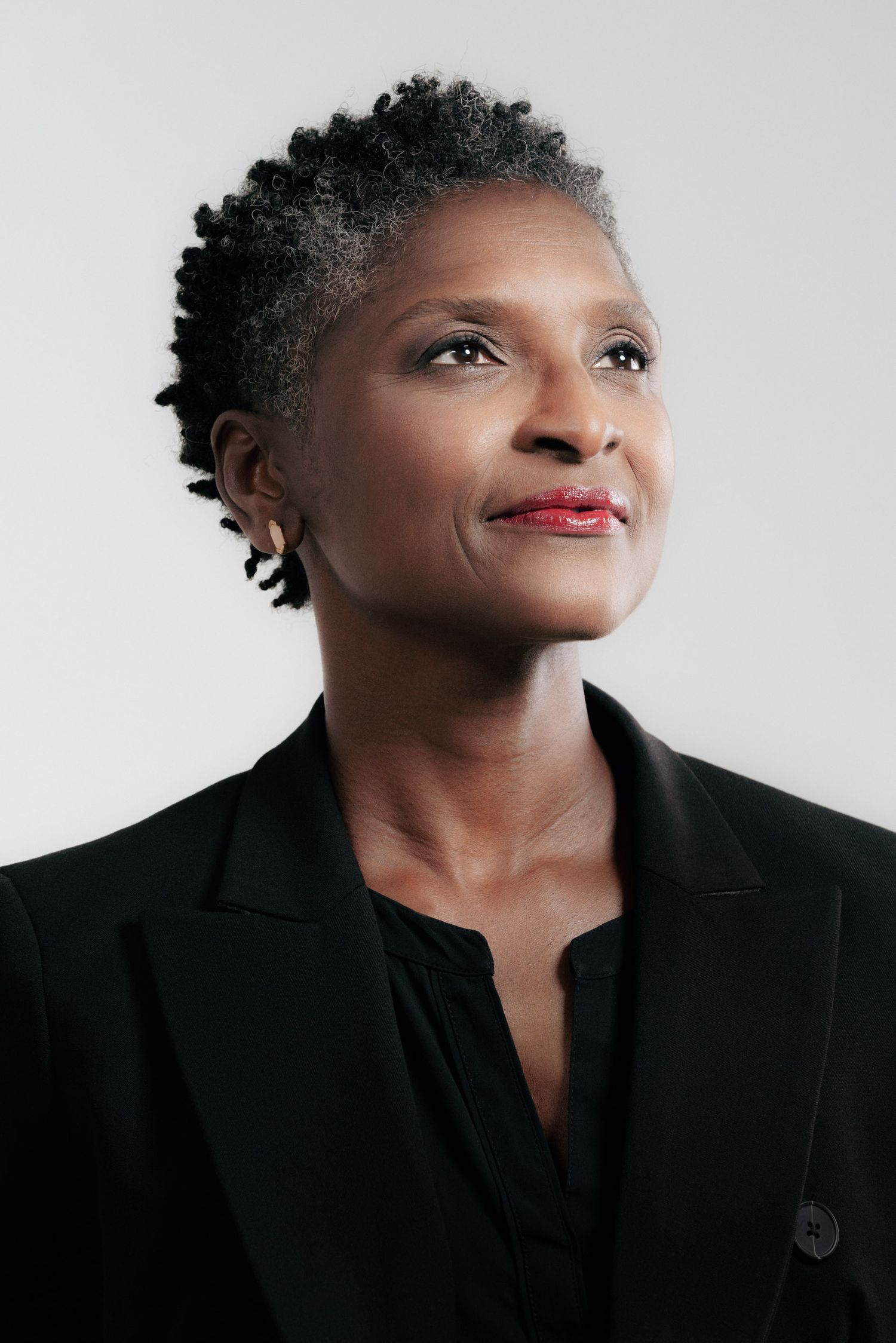 Professional studio portrait of a person with natural gray hair wearing a black blazer against a light background.