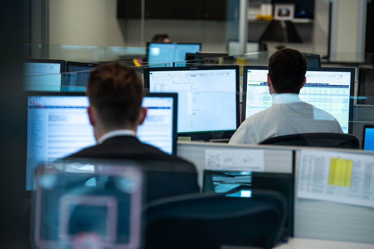 Business professionals working at multiple computer monitors in a modern office environment.