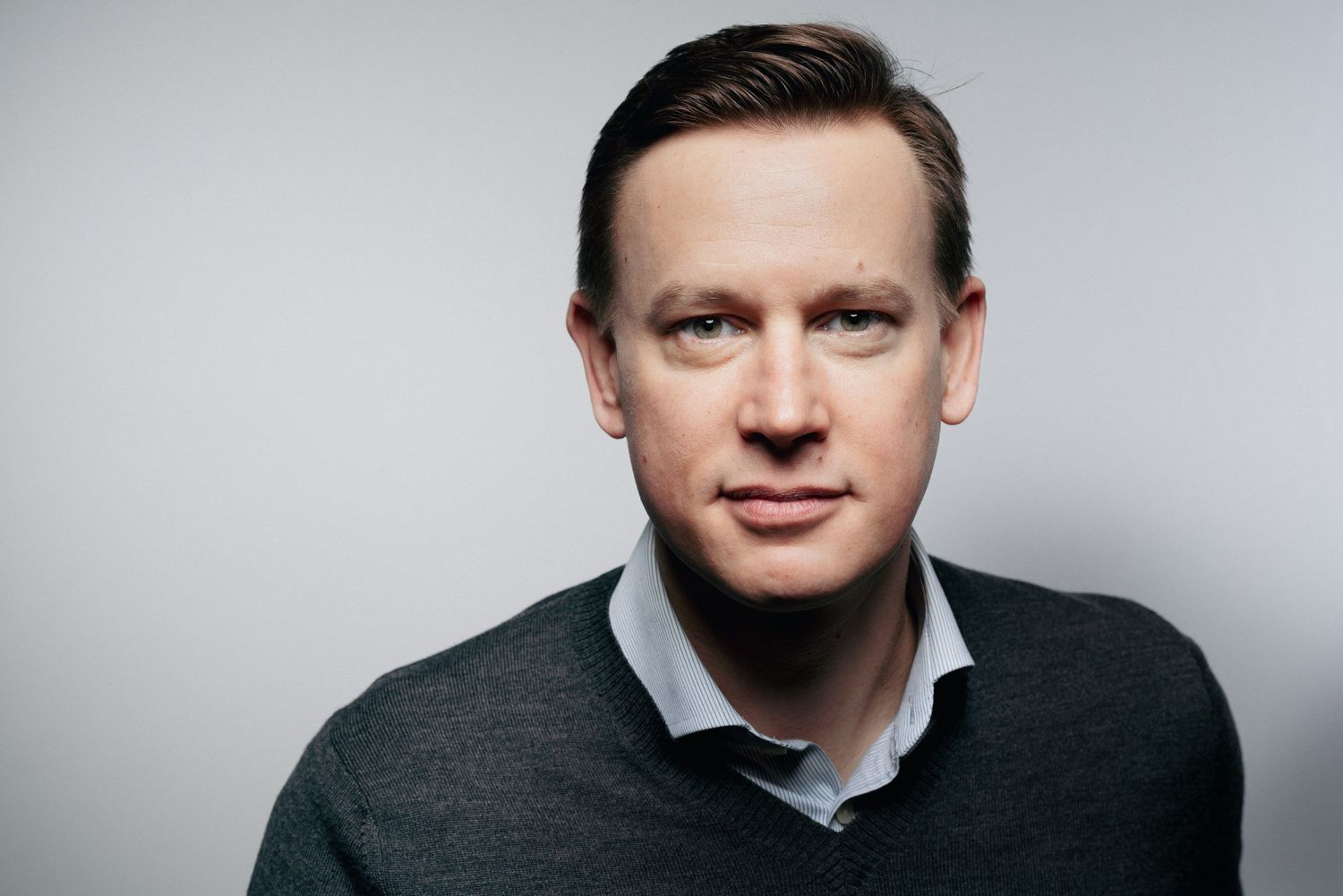 Professional headshot portrait of person in dark suit against light gray background.