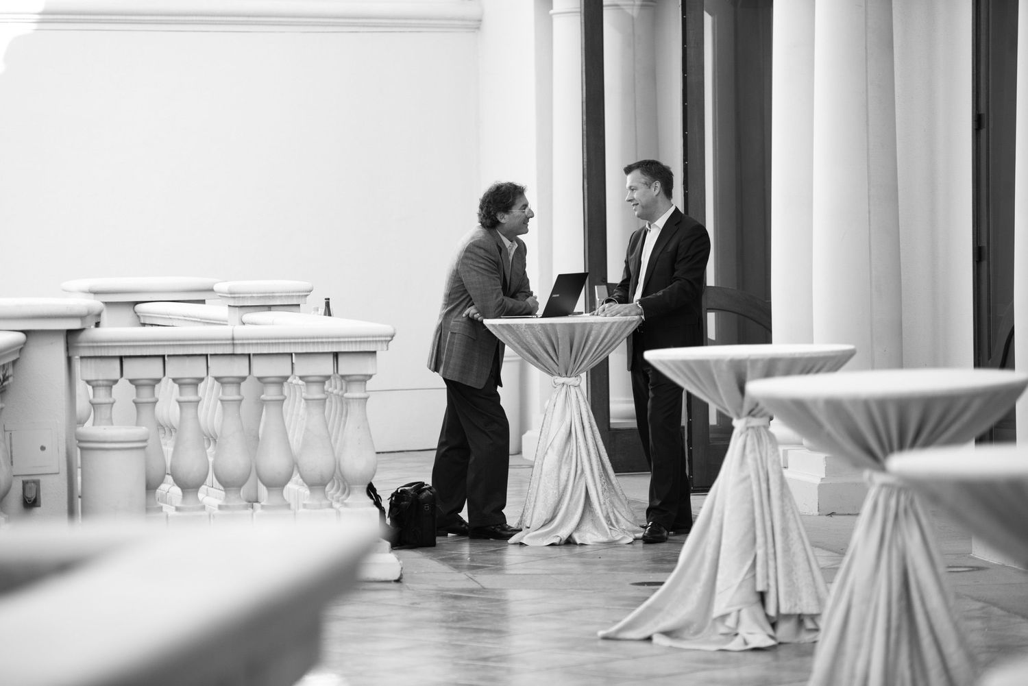 Black and white image of elegant cocktail tables with white linens in a formal event space.