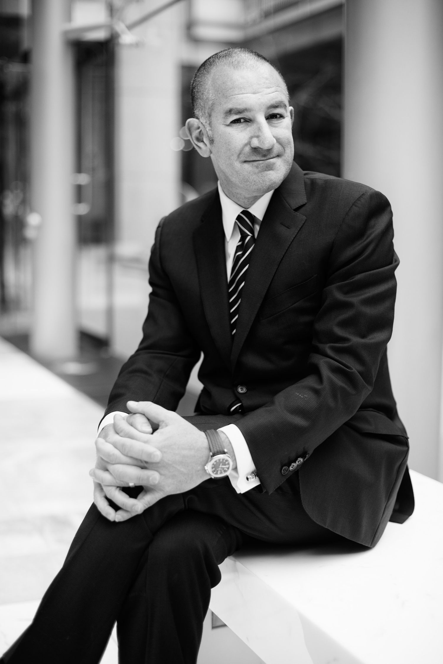 Black and white portrait of a business professional in a suit sitting casually on a ledge.