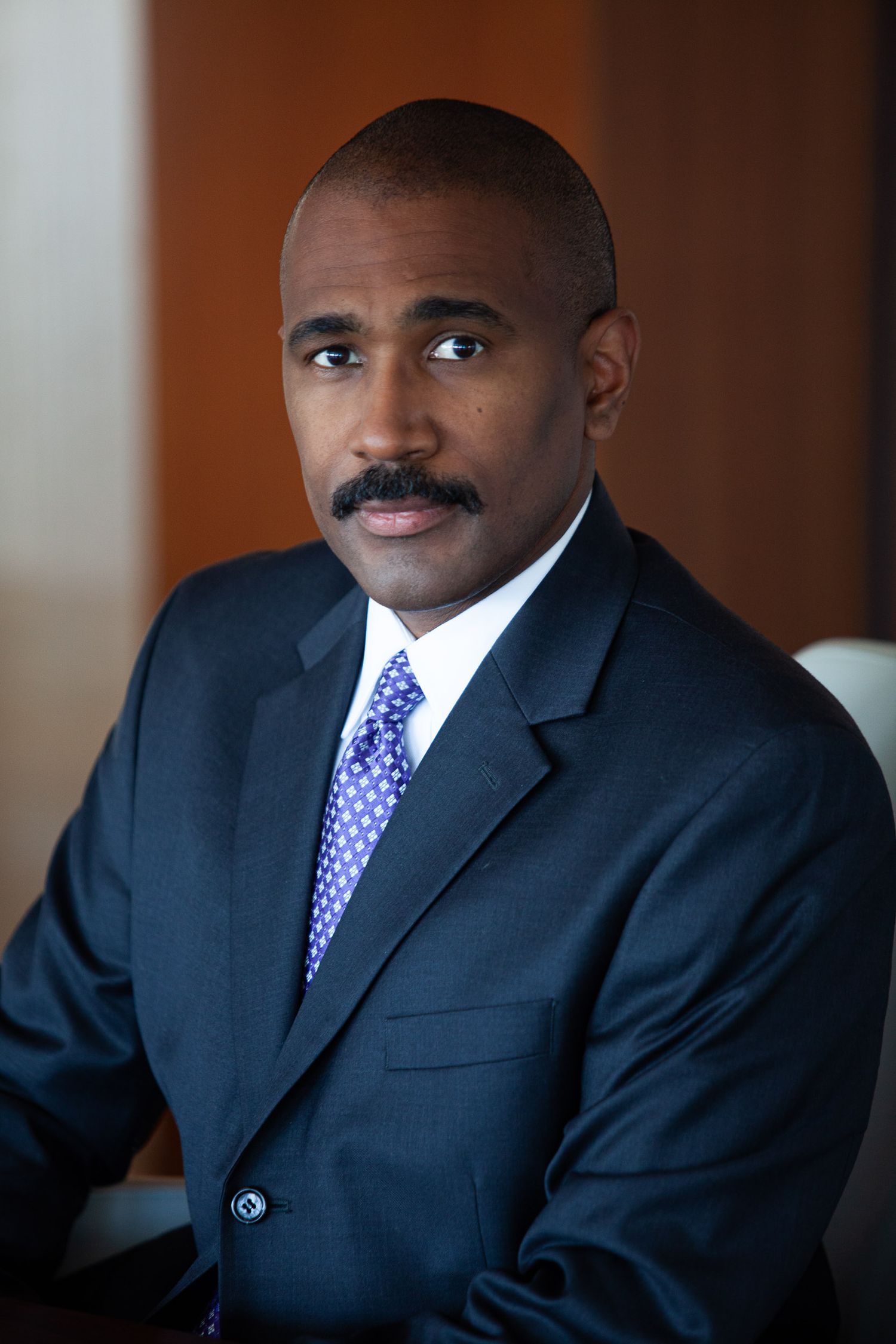 Professional headshots of someone in a navy suit and purple polka dot tie against a neutral backdrop.