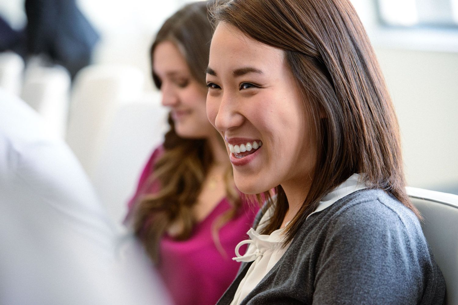 A group of people smile and laugh together while sitting in a bright modern office setting.