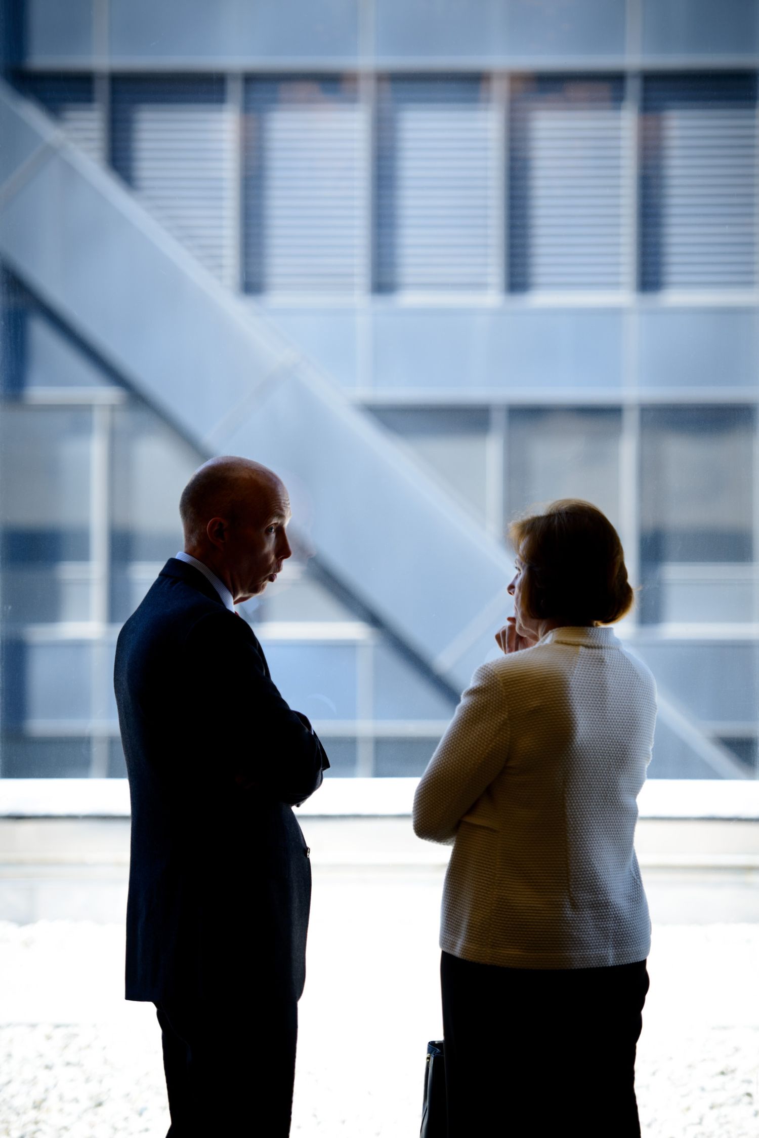 Two business professionals in silhouette having a conversation in front of a modern office window with diagonal beams.