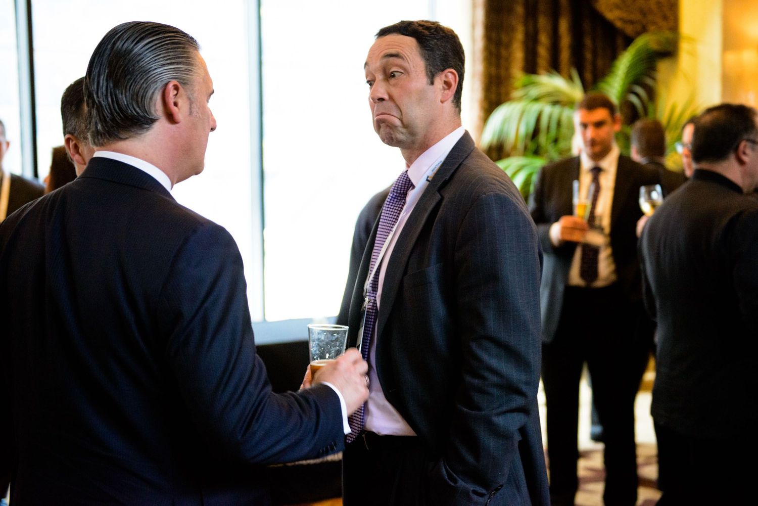 Business professionals in dark suits engage in conversation during a networking event in an office setting.