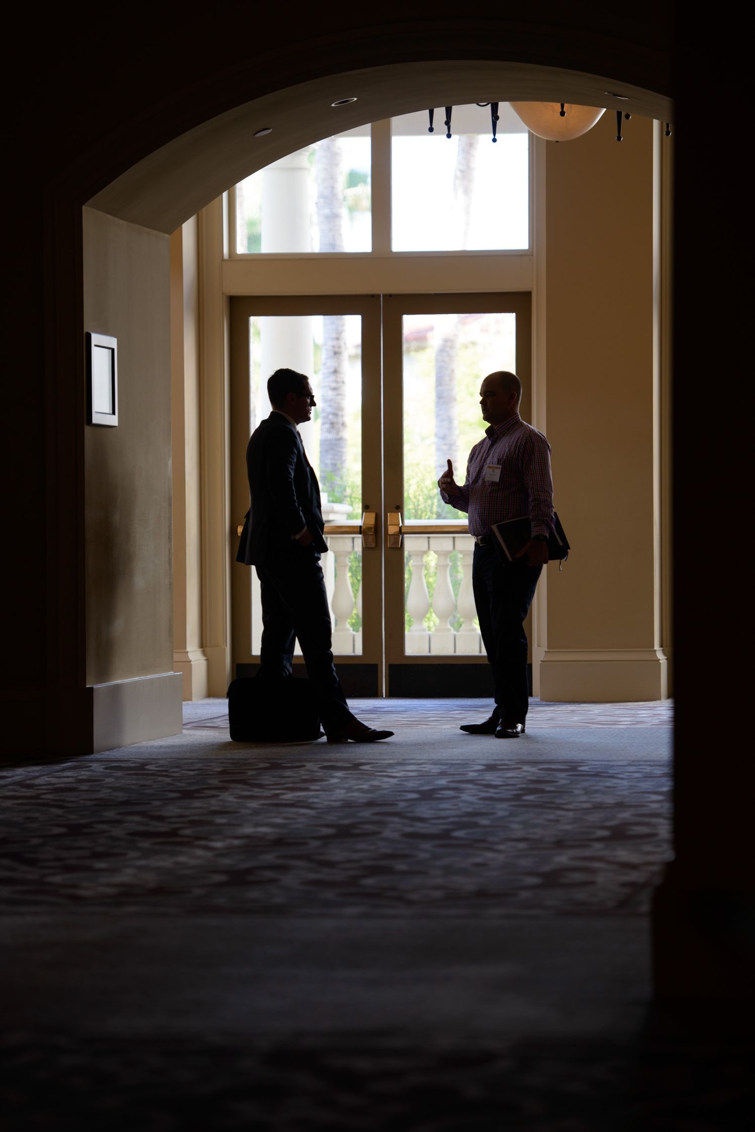 Silhouettes of people standing in a hallway with arched windows and carpeted floor.