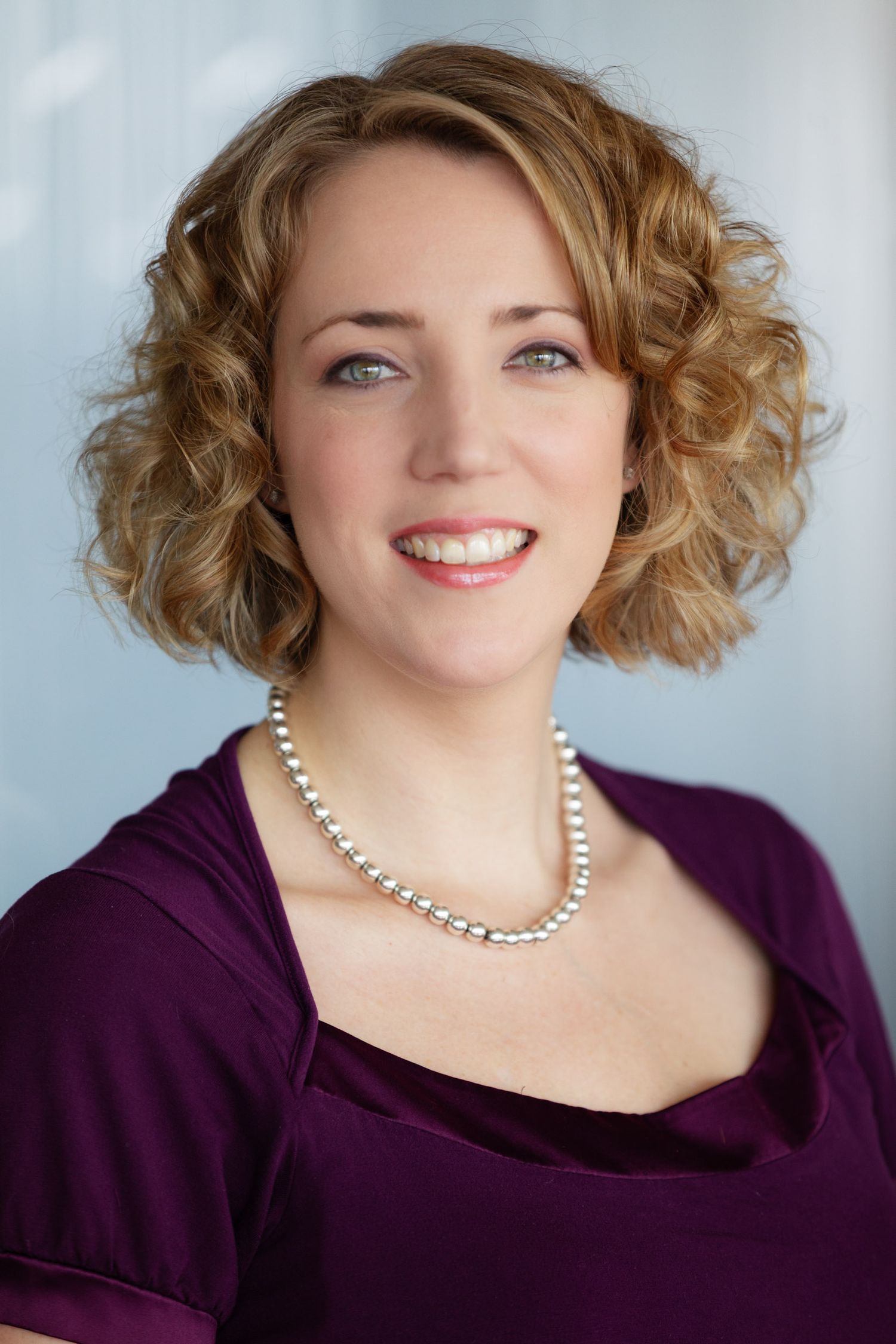 Professional headshot series showing different poses in a purple top with pearl necklace against light background.