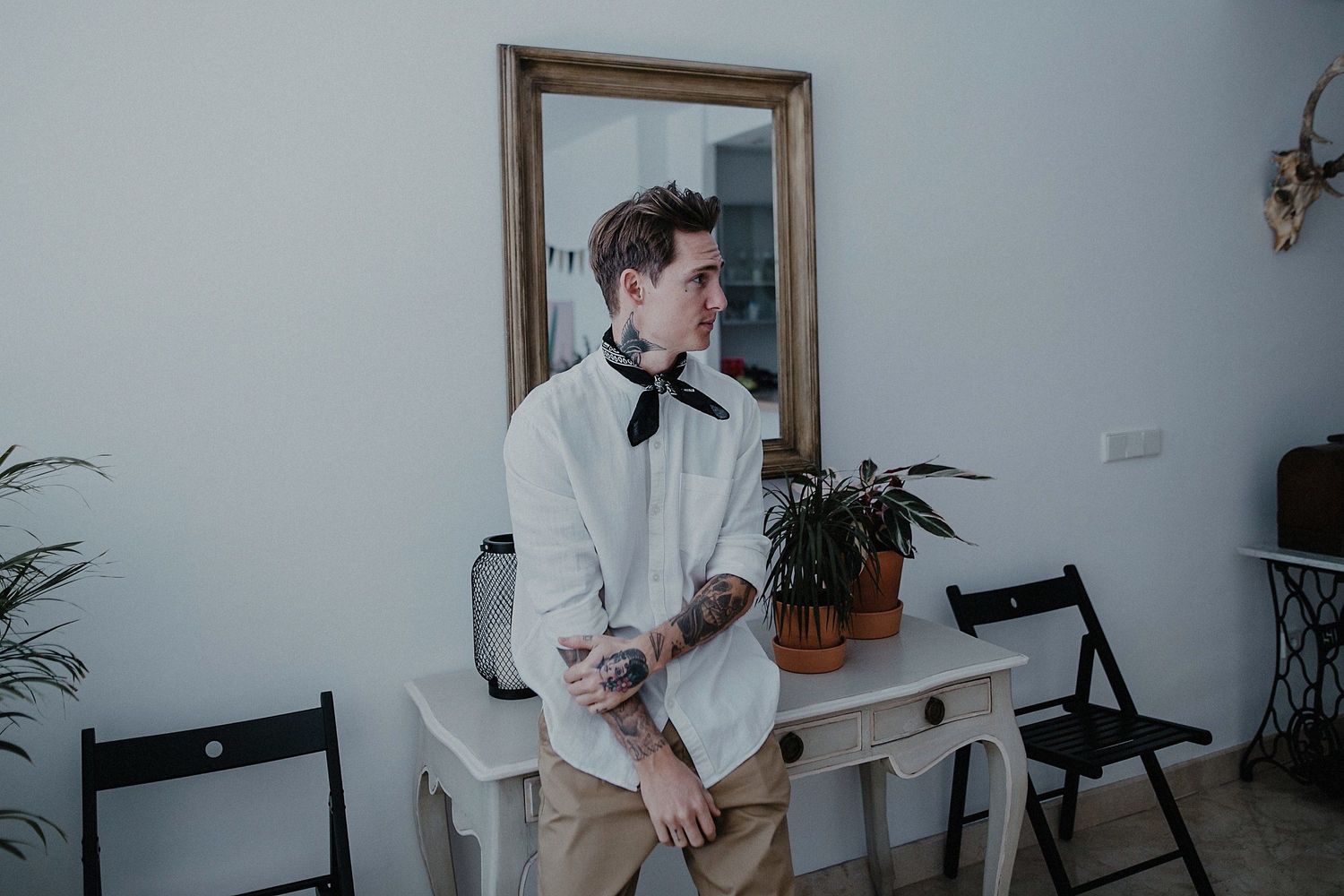 A person in white formal wear standing by a console table with a mirror.