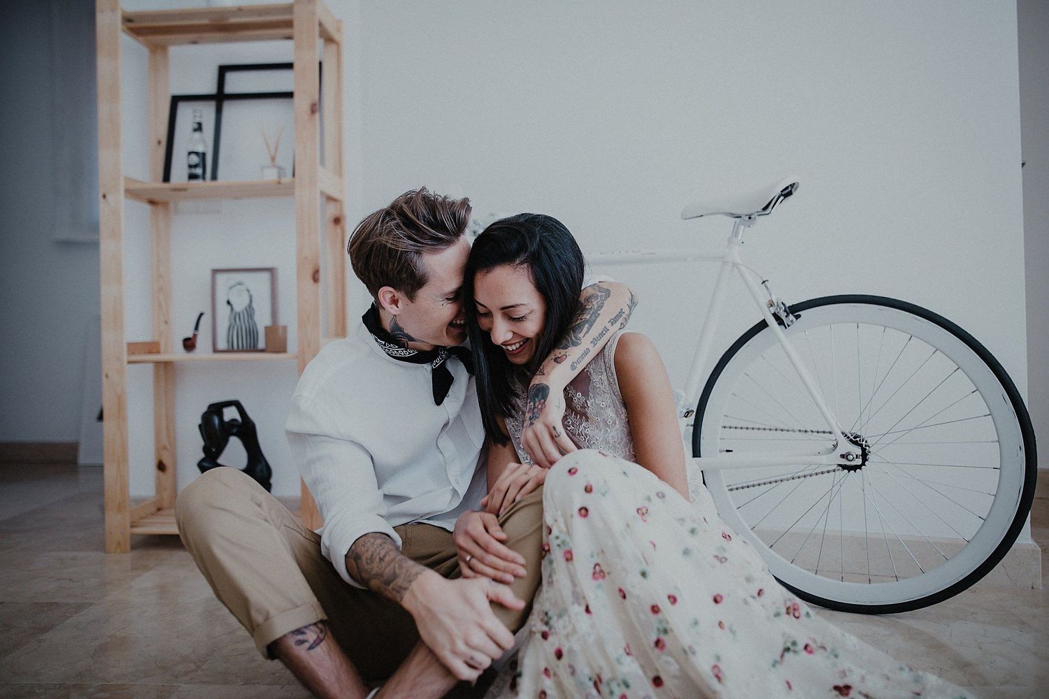 Intimate indoor portrait with wooden shelving and white bicycle as backdrop.
