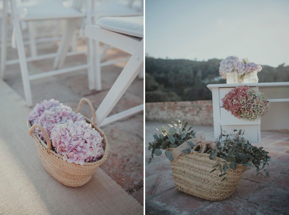 Pink flowers in woven baskets decorating outdoor wedding chairs.