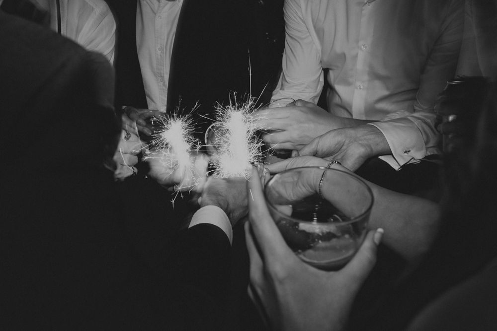 Black and white photo of hands holding sparklers creating bright trails of light.