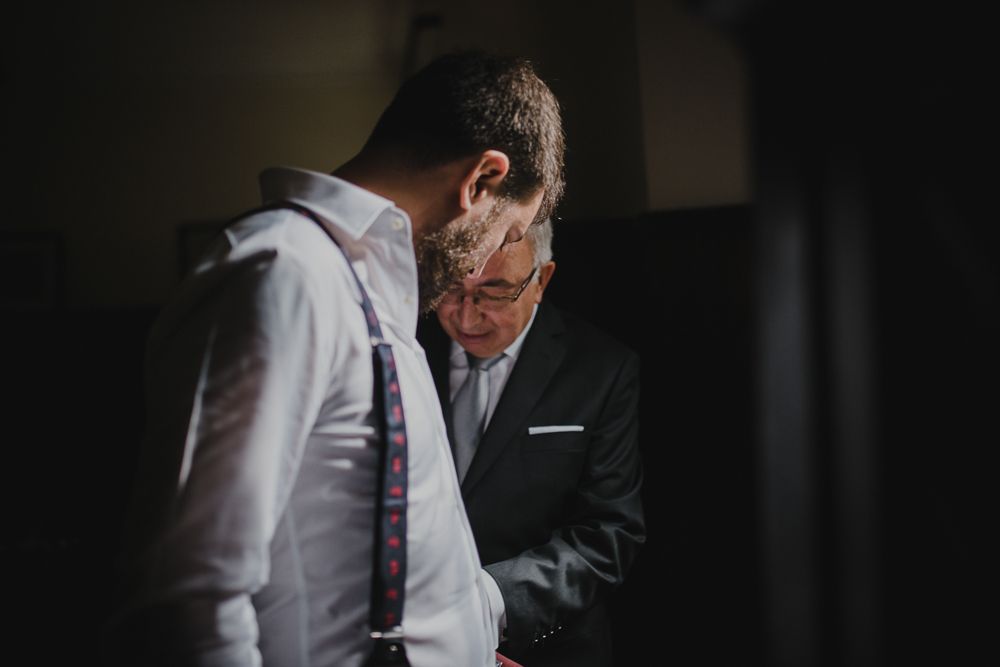 Two people in formal attire stand close together in a dimly lit room.