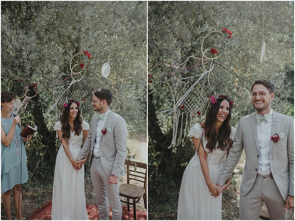 Outdoor wedding ceremony with couple dressed in grey suit and white dress in rustic garden setting.
