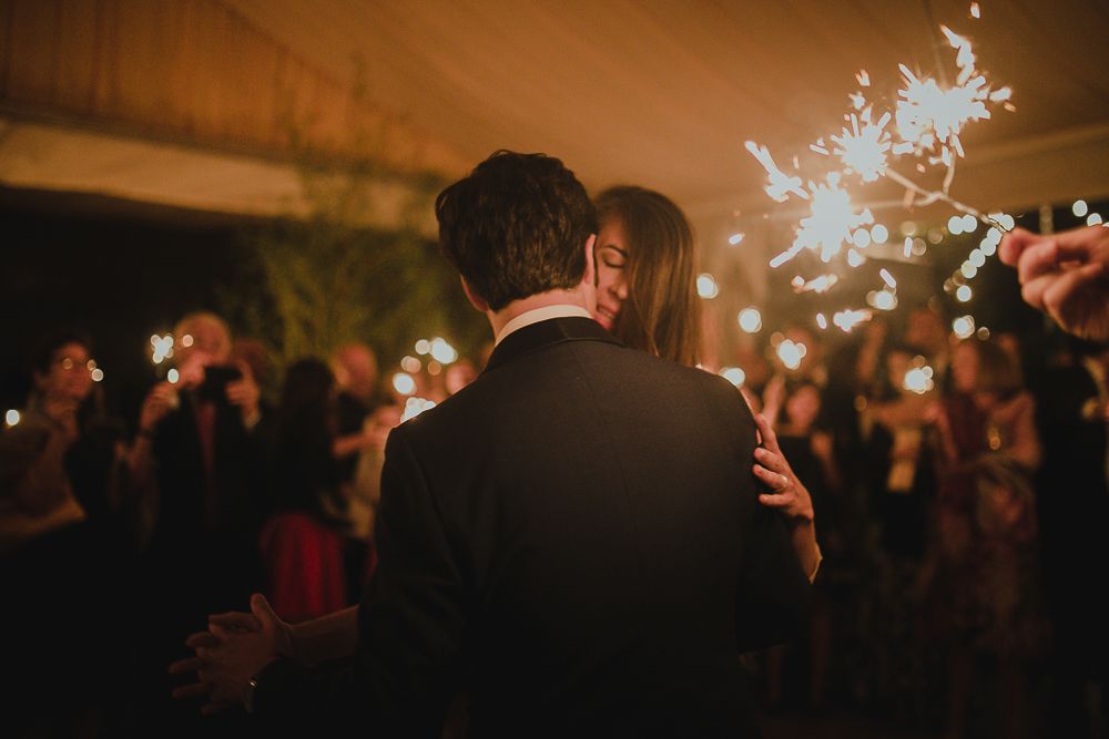 A couple embraces during their wedding sparkler celebration at night.