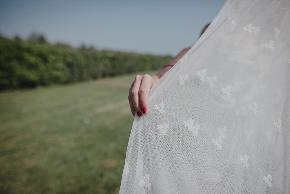 Detail shot of white wedding dress fabric against green landscape.