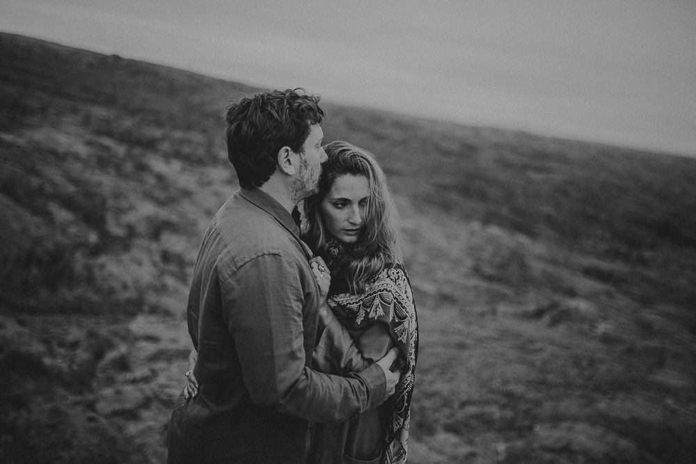 A moody black and white portrait of two people sharing a close moment on rugged terrain.