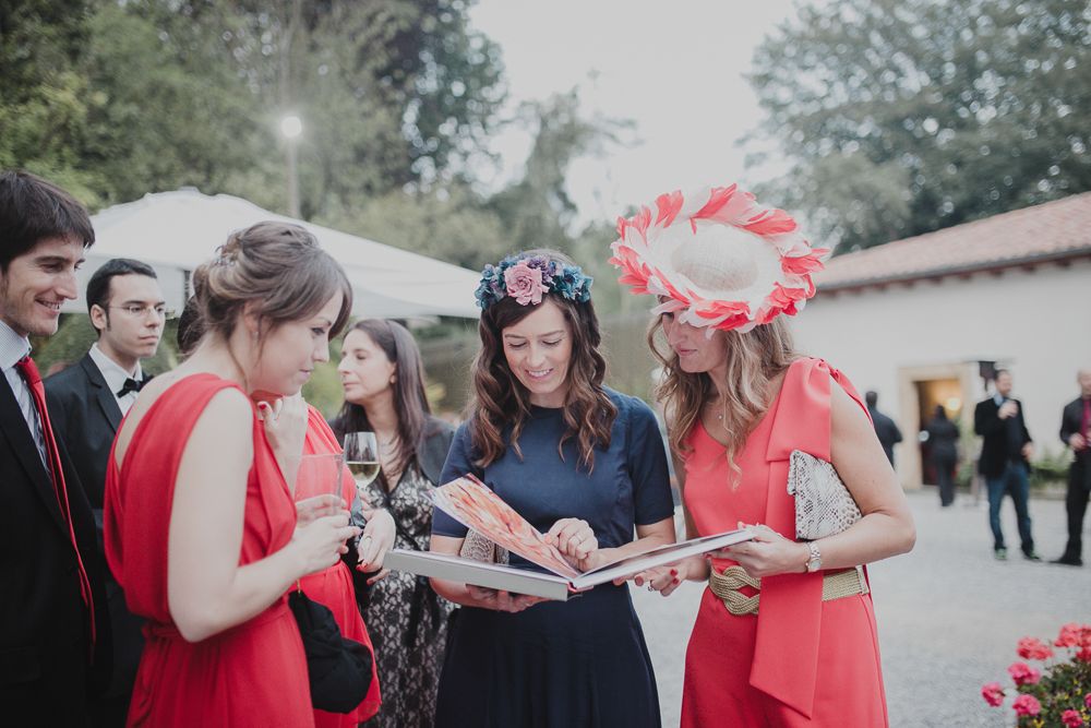 Wedding guests in coral dresses gather to look at something together under an umbrella.