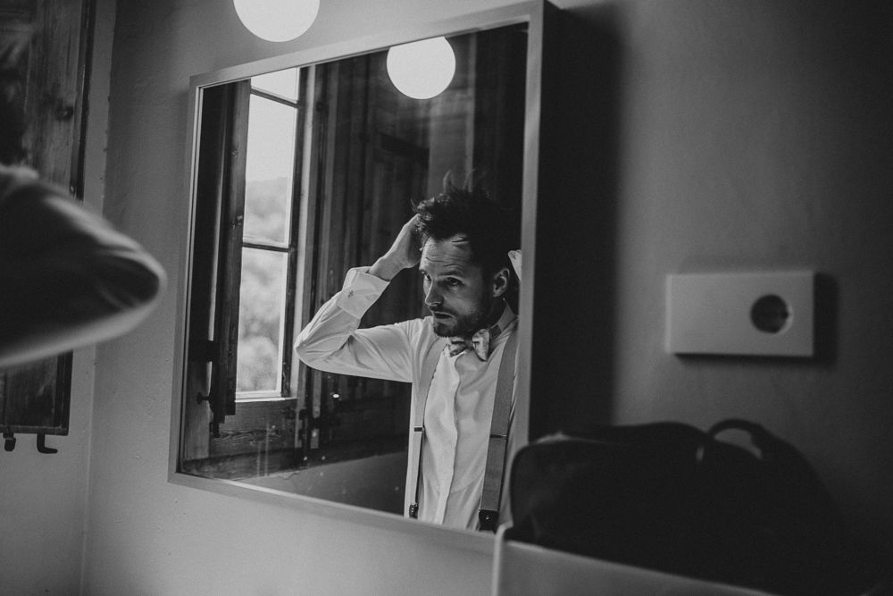 Black and white photo of person adjusting hair in mirror reflection.