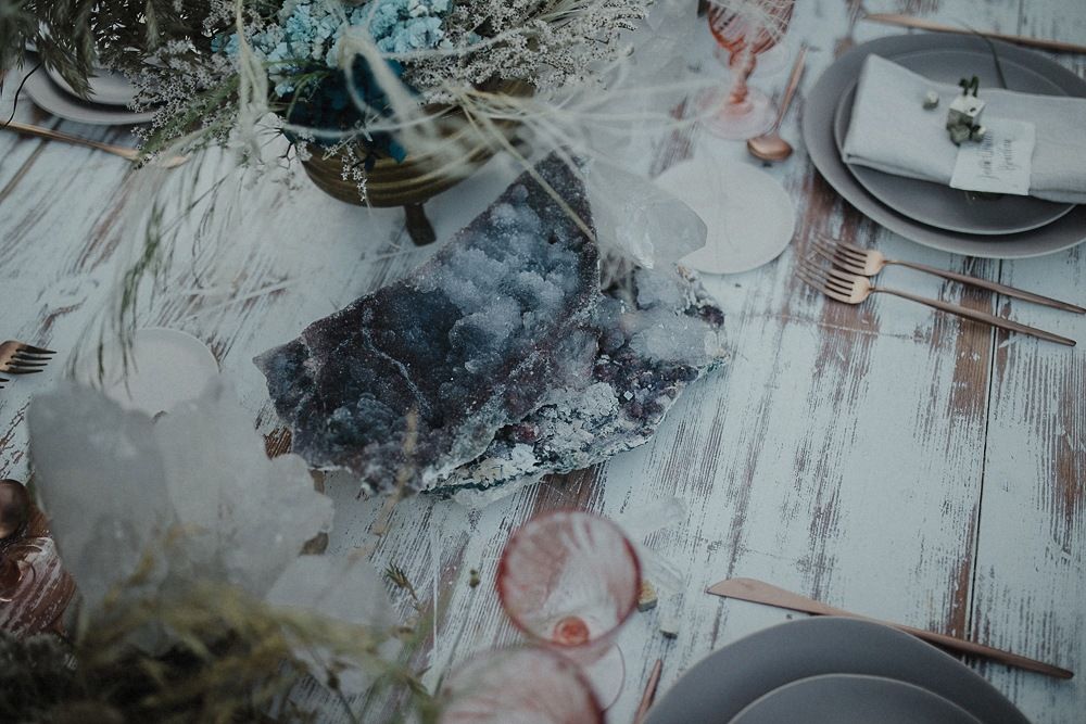 Rustic wedding table setting with pink glassware and dreamy details on a whitewashed wooden surface.