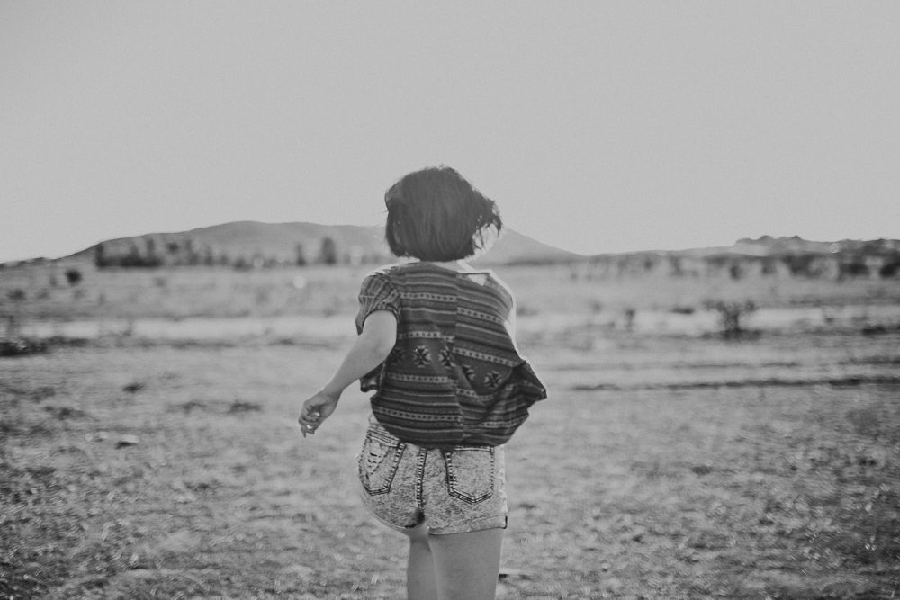 A silhouette of a small child looking out across a desert landscape in black and white.