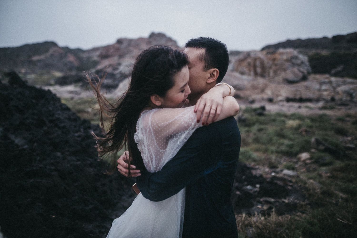 A couple embraces passionately against a rugged mountain landscape.