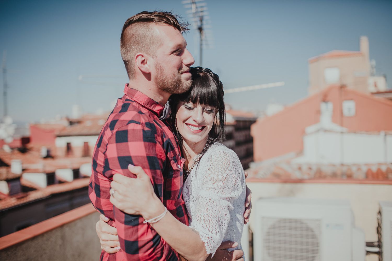 A sweet embrace on a sunny rooftop with classic Mediterranean architecture in the background.