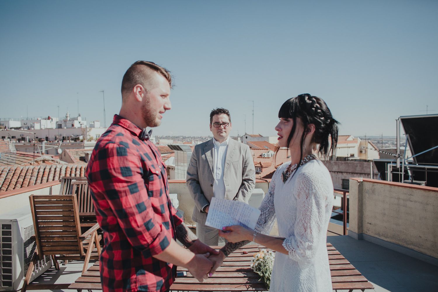 Intimate rooftop ceremony between three people under blue sky.