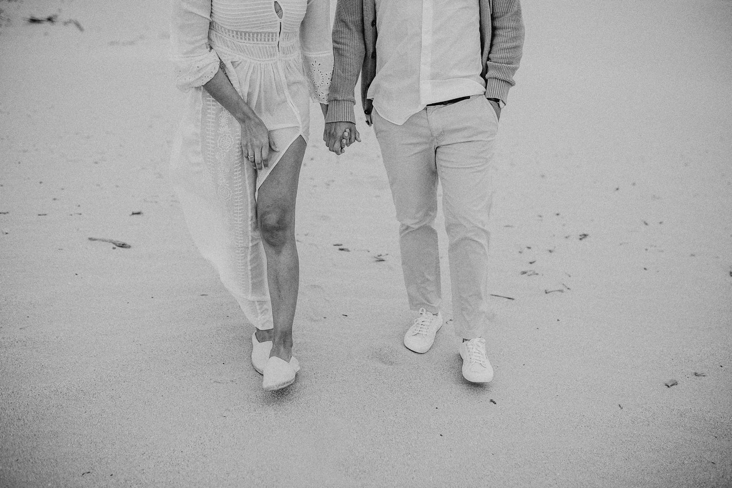 Lower body shot of couple wearing white and beige casual outfits on beach.