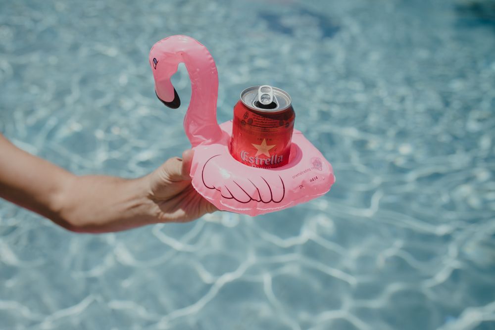Pink flamingo drink float holding a soda can in swimming pool water.