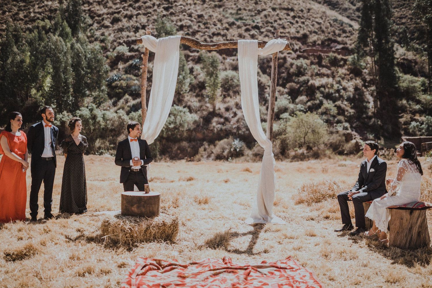 A rustic outdoor wedding ceremony setup with white fabric draped archway and wooden seating in a desert landscape.
